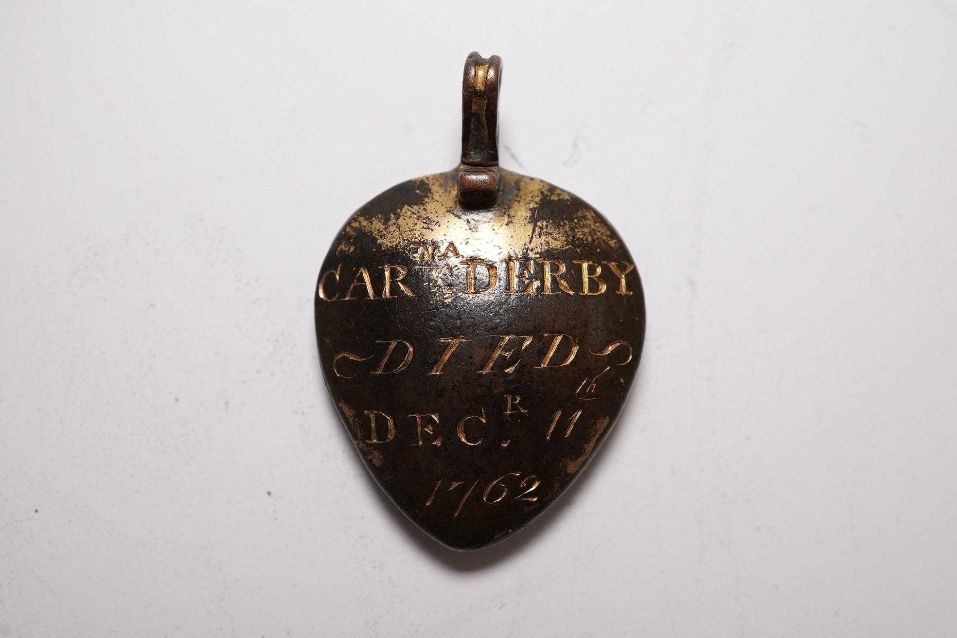 An 18th century gilt metal heart shaped mourning pendant, with engraved inscription, 'CARna DERBY DIED DEC 11th, 1762' and plaited hair beneath a glazed panel verso, 27mm.